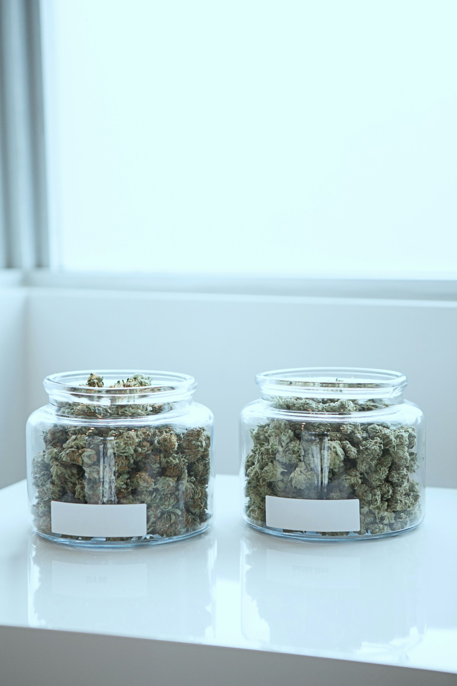 Two clear glass jars of labeled cannabis flower on a clean white counter