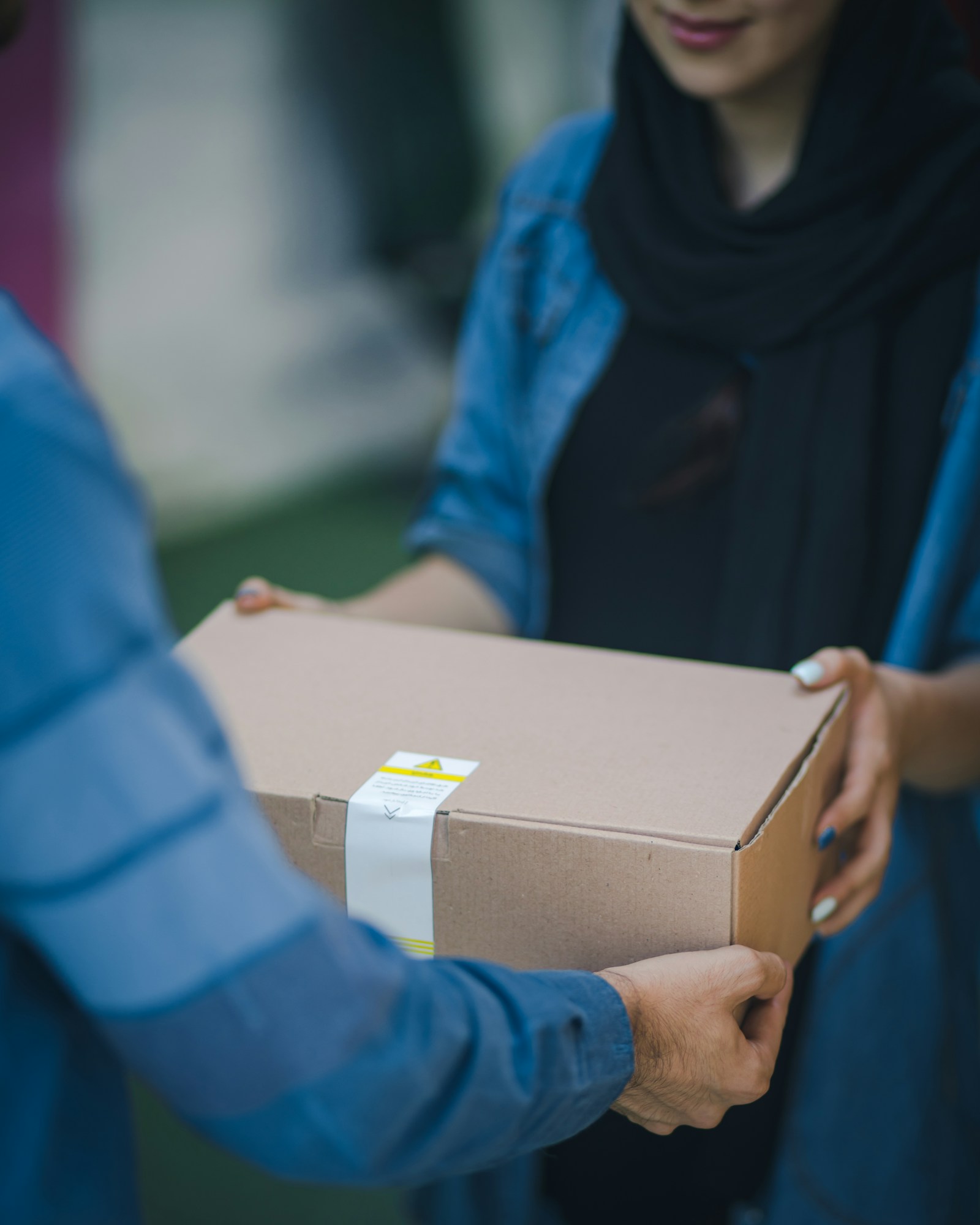 A plain cardboard package handed from a delivery driver to a customer at their door