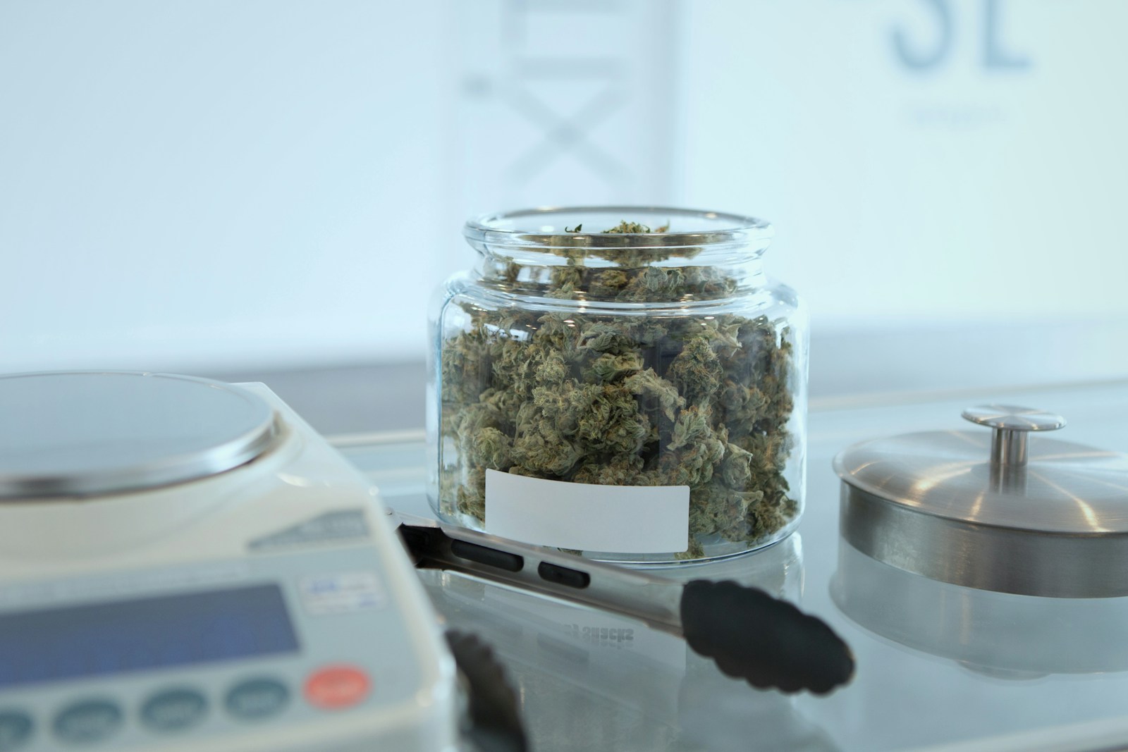 A labeled glass jar of cannabis flower on a precision scale in a lab setting